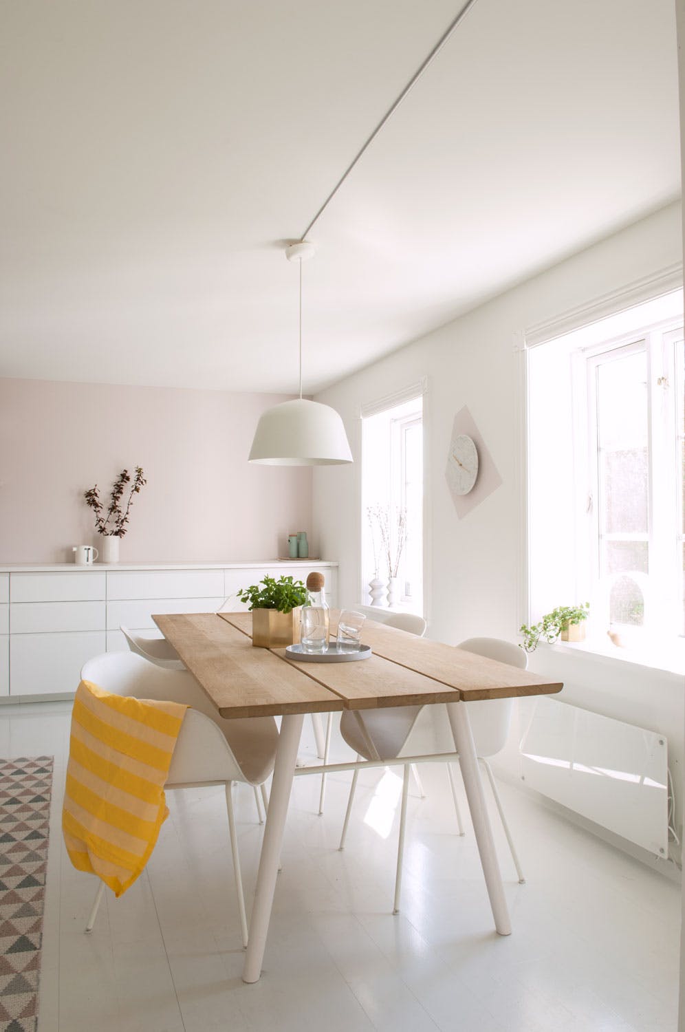 En rosa tråd Spisestoler og lampe fra Muuto, spisebord fra Woud, blomsterpotte fra Ferm Living og klokke fra Menu. Den lyse rosafargen på kjøkkenveggen er Perle FR1152 fra Fargerike.